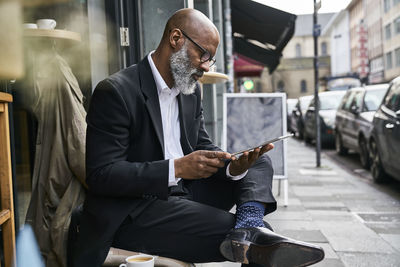 Mature businessman sitting in cafe using digital tablet