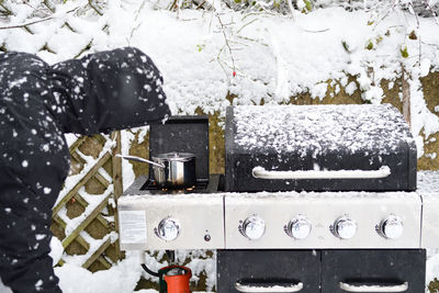 Person wearing warm clothing by barbecue in back yard during winter