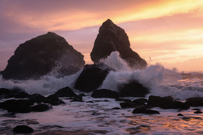 Rocks in sea against sky during sunset
