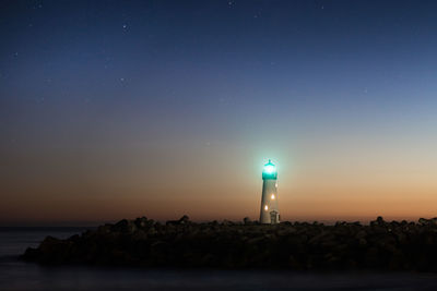 Lighthouse by sea against clear sky at night