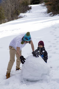 Cheerful brothers making snowman during winter