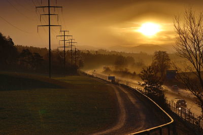 Road by trees against sky during sunset