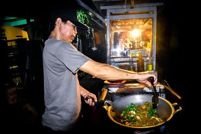 Side view of chef preparing food at market stall during night