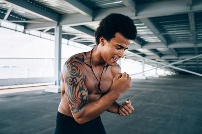 Shirtless male boxer exercising below bridge