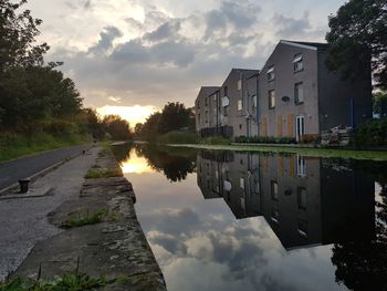 Reflection of houses and trees by lake against sky during sunset