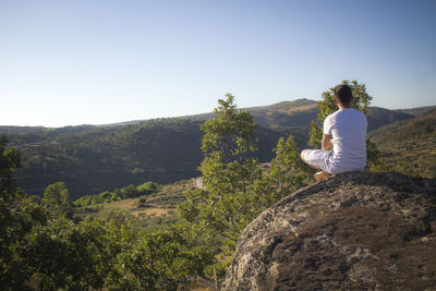 Rear view of woman sitting on rock against clear sky