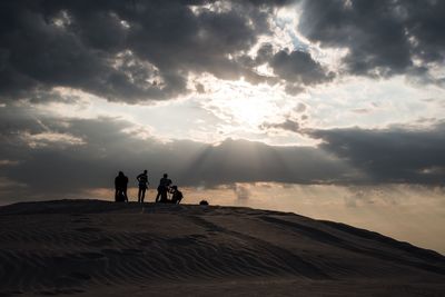 Silhouette of people on landscape against cloudy sky