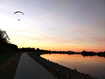Scenic view of paraglider flying over lake at sunset