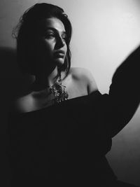 Young woman looking away while standing against wall