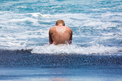 Rear view of man sitting in sea