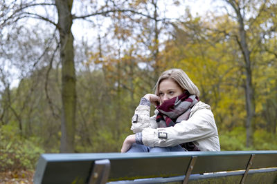 Young woman looking away sitting on bench at park 