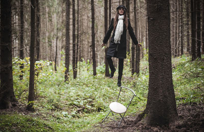 Woman balancing on chair against trees in forest