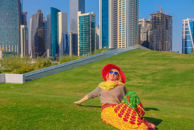 Woman sitting on field against modern buildings