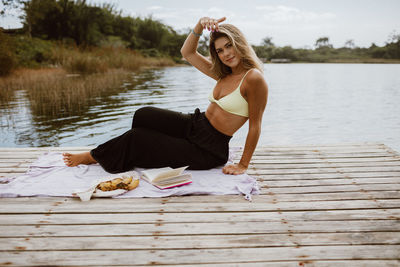 Young woman sitting on pier over lake