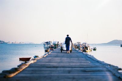 Rear view of man walking by sea against clear sky