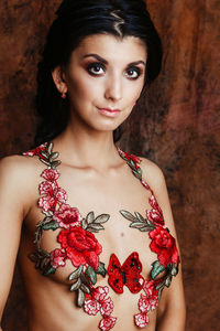 Portrait of shirtless young woman with floral decoration standing against wall