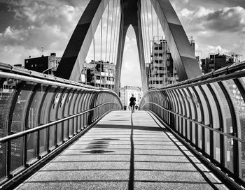 People walking on footbridge in city against sky