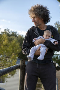 Father looking away while carrying daughter against sky