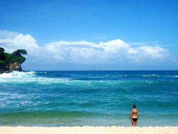 Rear view of woman standing on beach against blue sky