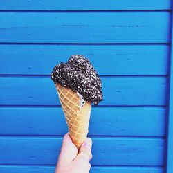 Cropped hand of woman holding ice cream cone against wall