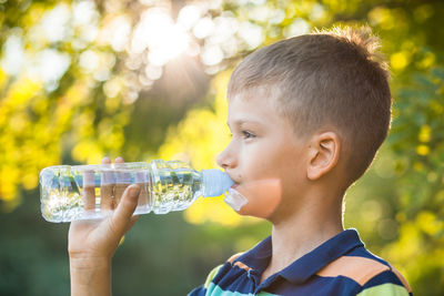 Side view of smiling boy drinking water while standing outdoors