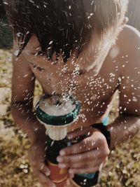 Close-up of shirtless boy holding water hose while standing in yard