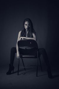 Portrait of beautiful fashion model sitting on folding chair against black background
