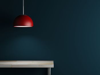 Illuminated red pendant light hanging over wooden table by blue wall