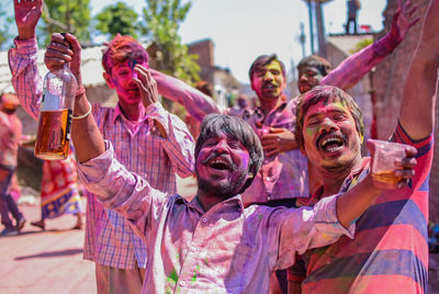 Portrait of happy friends with drinks enjoying on street during holi