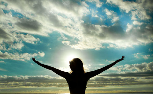 Rear view of woman with arms outstretched against cloudy sky