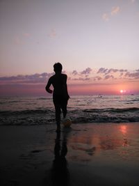 Rear view of boy playing with ball at beach during sunset