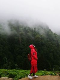 Woman wearing hood standing on rock against trees