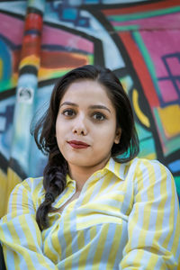 Portrait of smiling young woman against graffiti wall