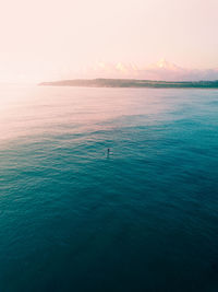 Scenic view of sea with man on surfboard against sky during sunset