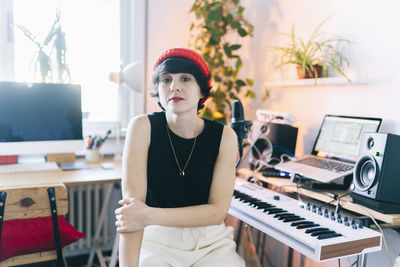 Female music composer wearing knit hat while sitting by electric piano in studio
