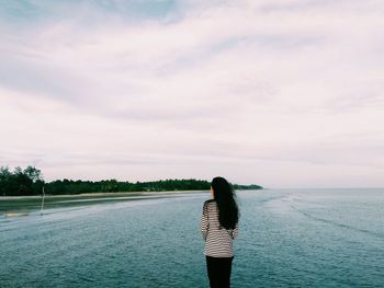 Rear view of woman standing by sea against sky