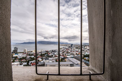 Cityscape by sea against sky seen through window