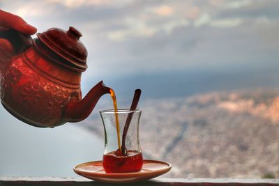Cropped hand pouring tea in glass on railing