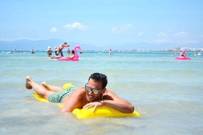 Shirtless young man relaxing on pool raft in sea against sky