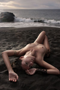 Naked woman lying down on sand at beach