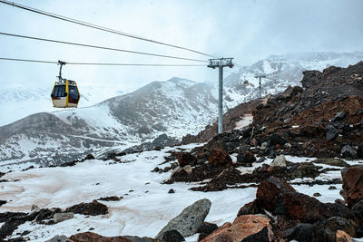 Ski lift over snow covered mountains against sky