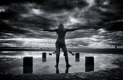 Rear view of man standing by wooden post in sea against sky