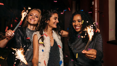 Smiling friends holding lit sparklers in party