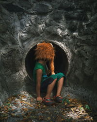 Full length of boy wearing animal mask sitting near pipe