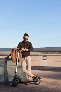 Young modern man wating in the park with electric scooter and entertained with the new smart watch