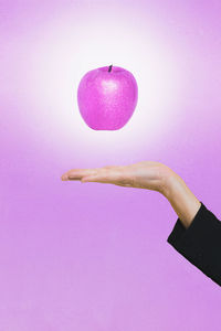 Close-up of hand with levitating apple against pink background