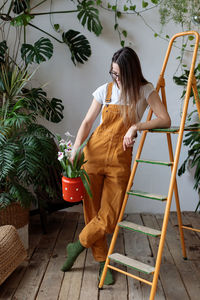 Young woman florist holding orchid flower in milk can while working in flower shop or plant store