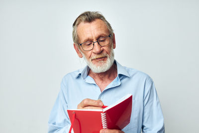 Senior man reading book against white background