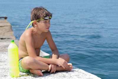 Shirtless boy sitting by sea