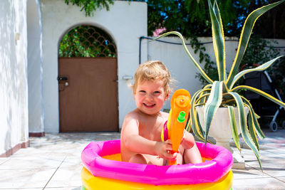 Cute baby is having fun in an inflatable pool with a water gun in summer.